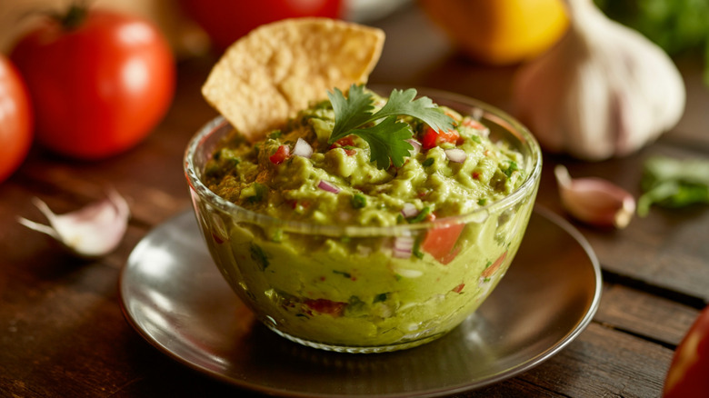 Guacamole Dip: mexican cuisine, guacamole bowl, tortilla chip, rustic wooden table, fresh ingredients, avocados