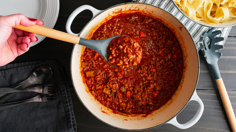 Hand holding serving spoon of Bolognese sauce