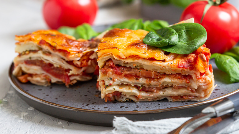Two pieces of lasagna on plate with basil, tomatoes
