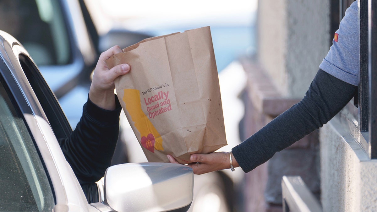 A customer grabs a McDonald's drive-thru bag from an employee.
