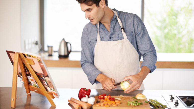 Man cooking in kitchen and following along with a cookbook in a stand