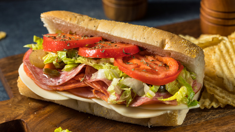 Whole Italian sub on wooden board with potato chips