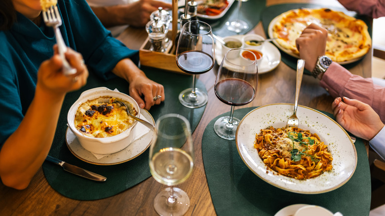 People eating various pasta dishes and drinking wine at a restaurant