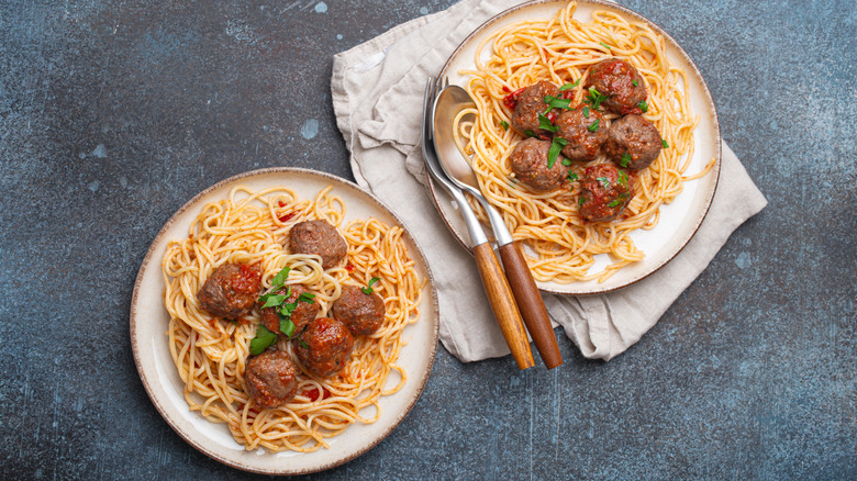 Two plates of spaghetti and meatballs with utensils and a napkin