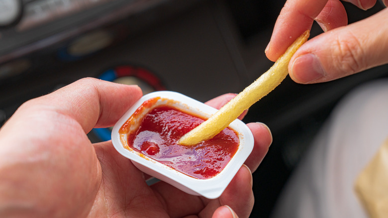 person dipping a McDonald's French fry into a ketchup packet