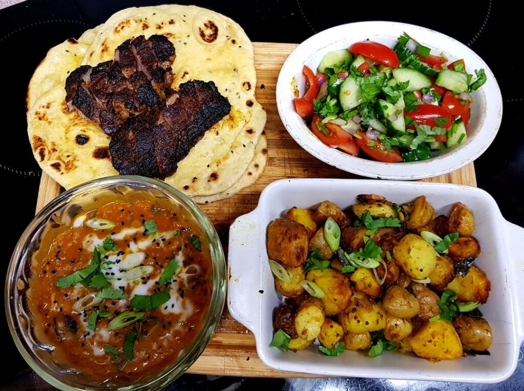Ugly Delicious. Charred Spiced Lamb Steaks, Tomato and Coconut Dhal, Spiced Potatoes, Cucumber Salad and Fresh Naan Breads.