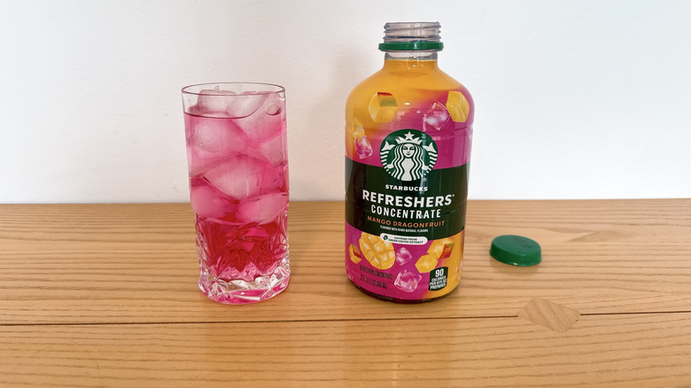 Starbucks Mango Dragonfruit Refreshers Concentrate bottle and poured into a glass