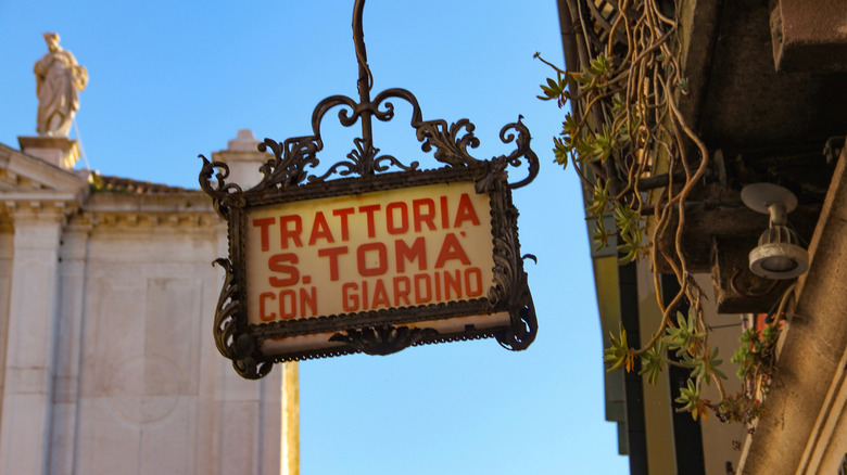 A sign for a trattoria hangs over a street in Venice, Italy