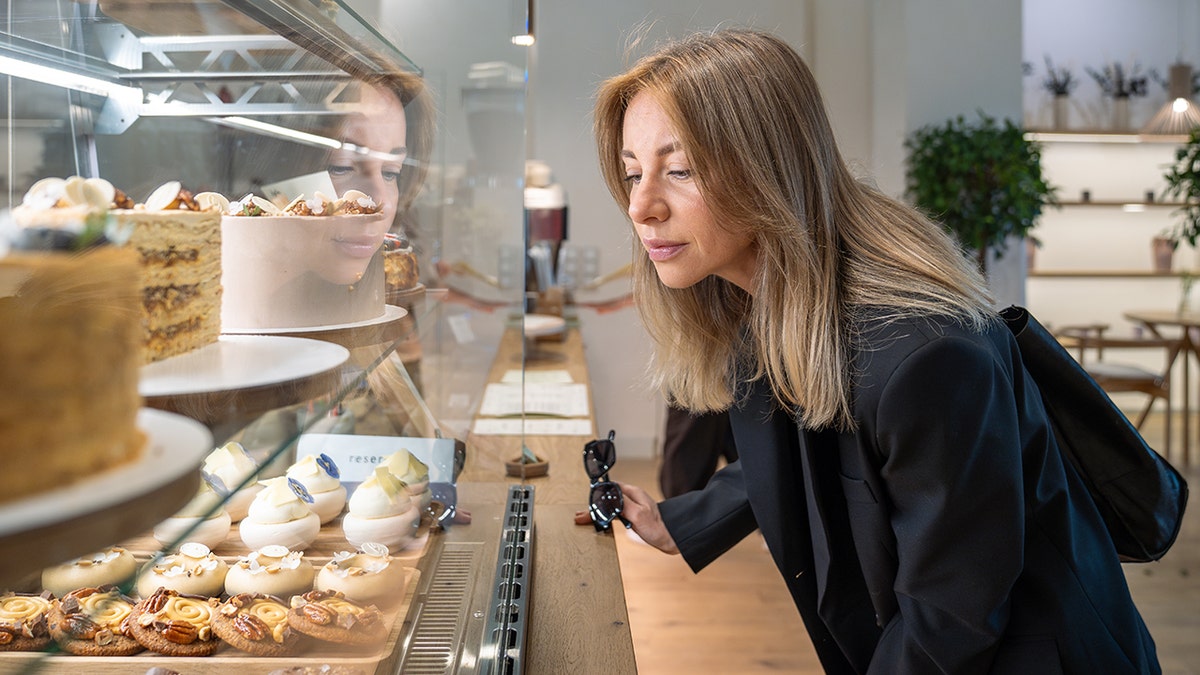 Woman looking at cakes and pastries inside a glass bakery display case.