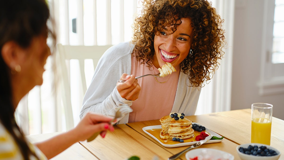 Woman eating a stack of pancakes with her friend at the table.