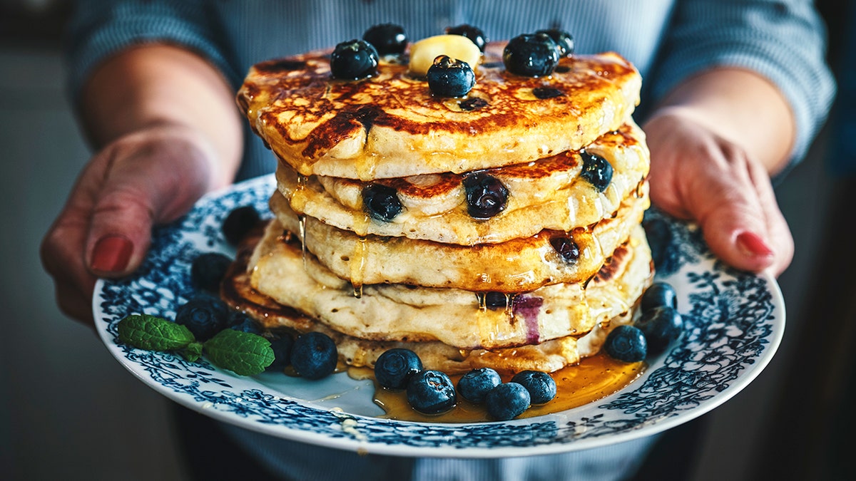 Woman holding a blue and white designed plate of blueberry pancakes.