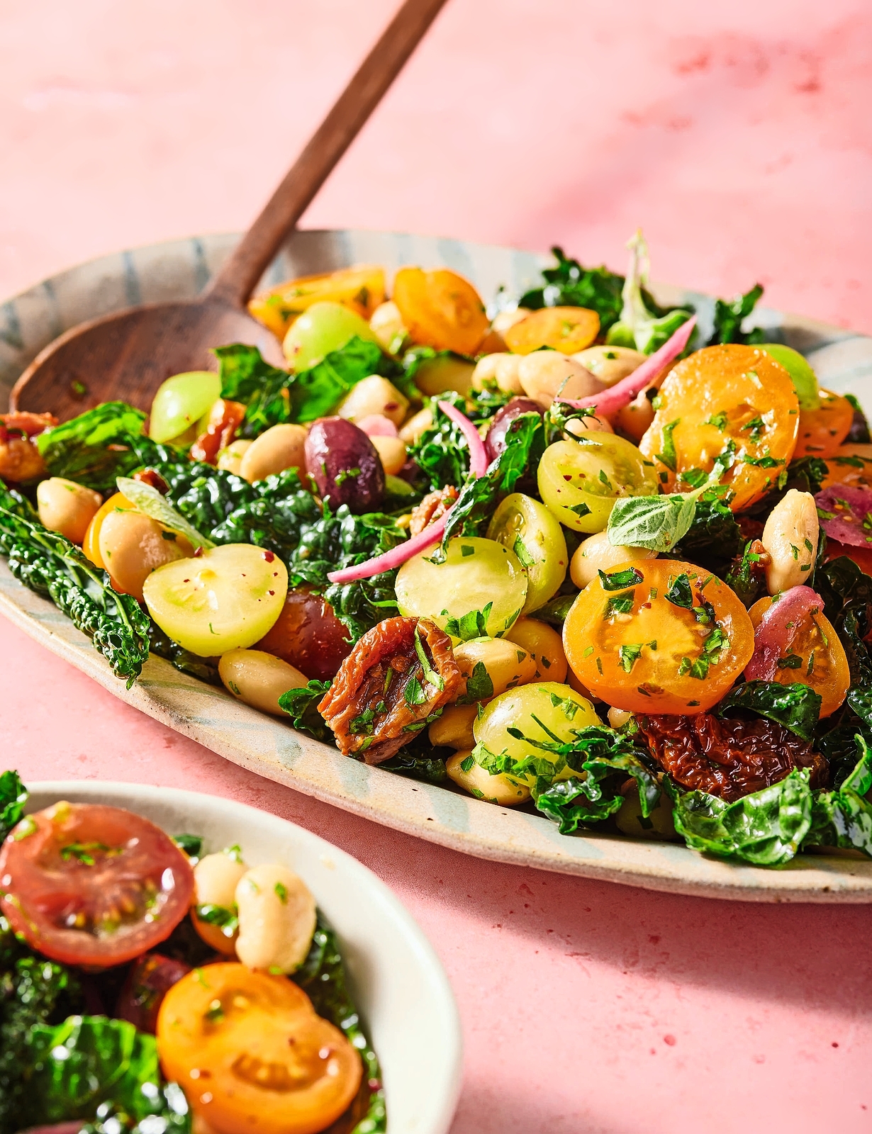 Cavolo Butter Bean salad with kale, cherry tomatoes, olives, and herbs, served in a long ceramic dish with a wooden spoon.