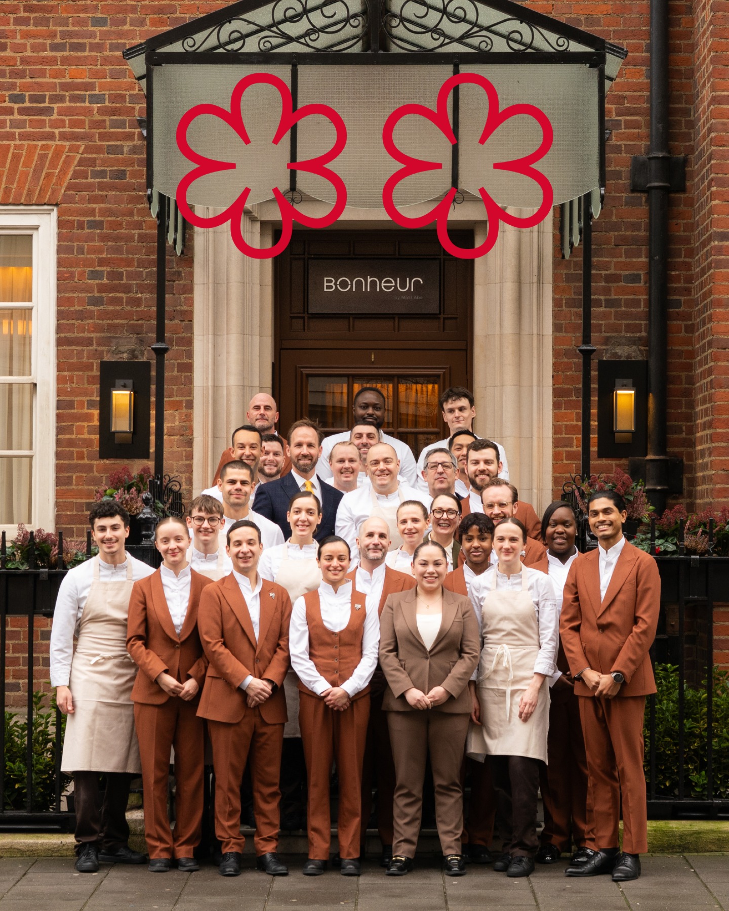 The staff of Bonheur by Matt Abé restaurant posing outside, with two Michelin stars overlaid on the building.