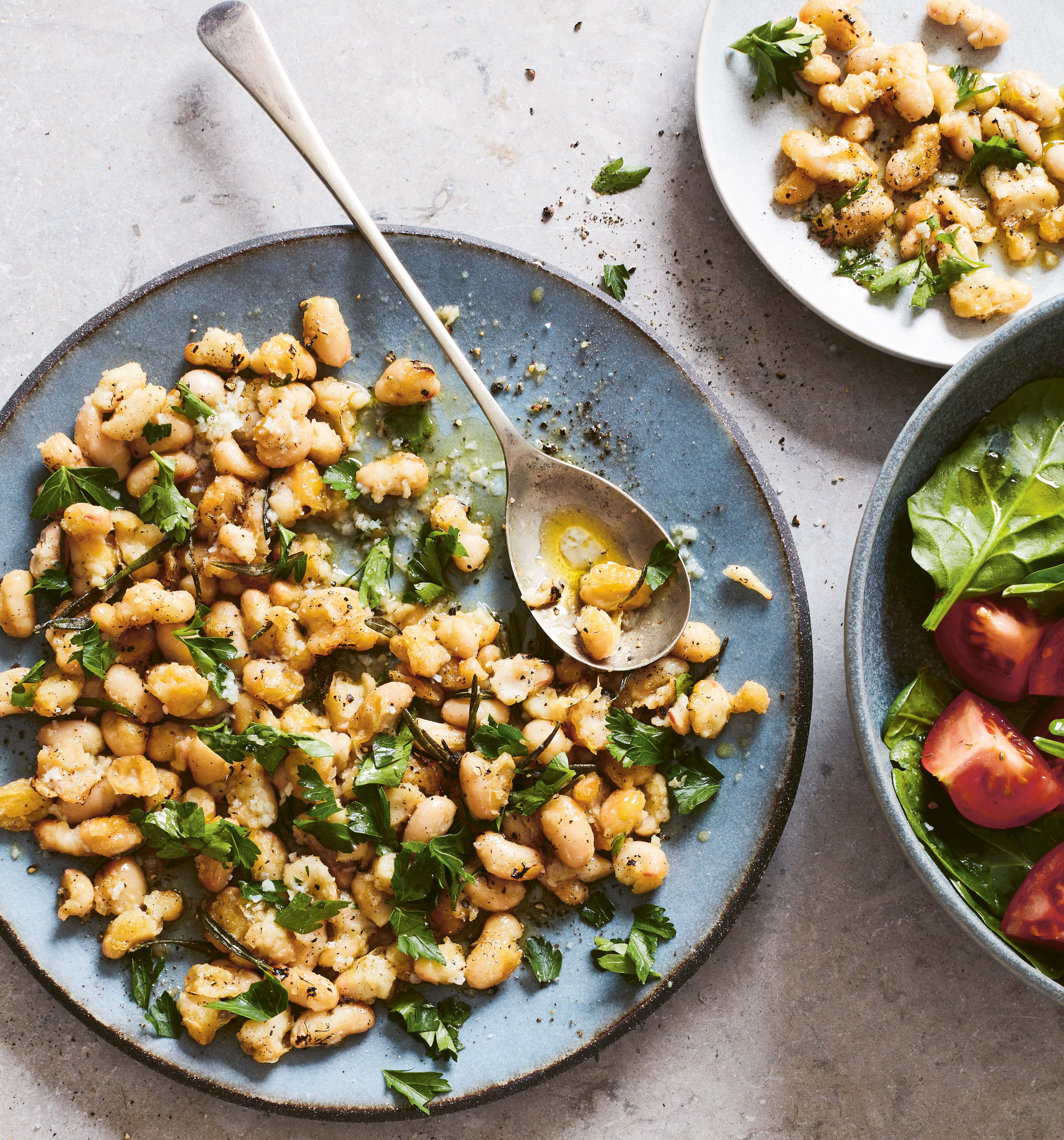 A plate of cannellini bean salad with herbs and a side of spinach and tomato salad.