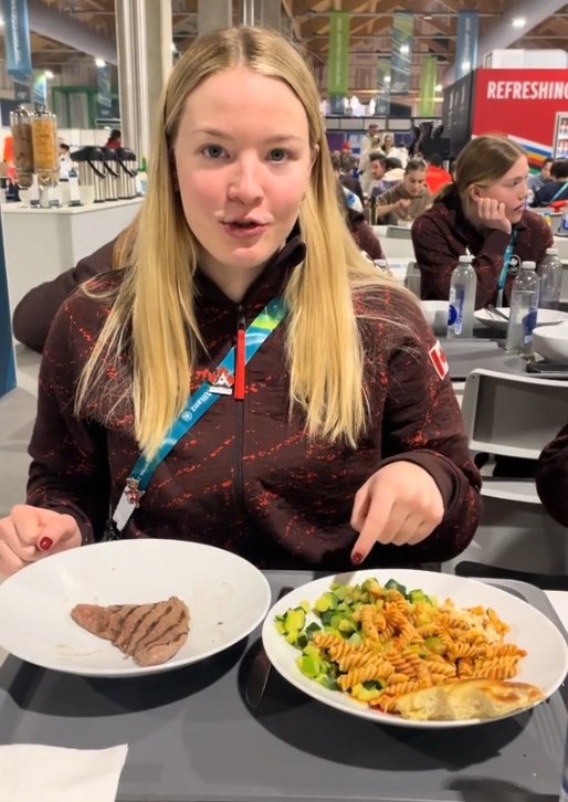 Julia Gosling showing a plate of meat and a plate of pasta with vegetables at the Winter Olympics dining hall.