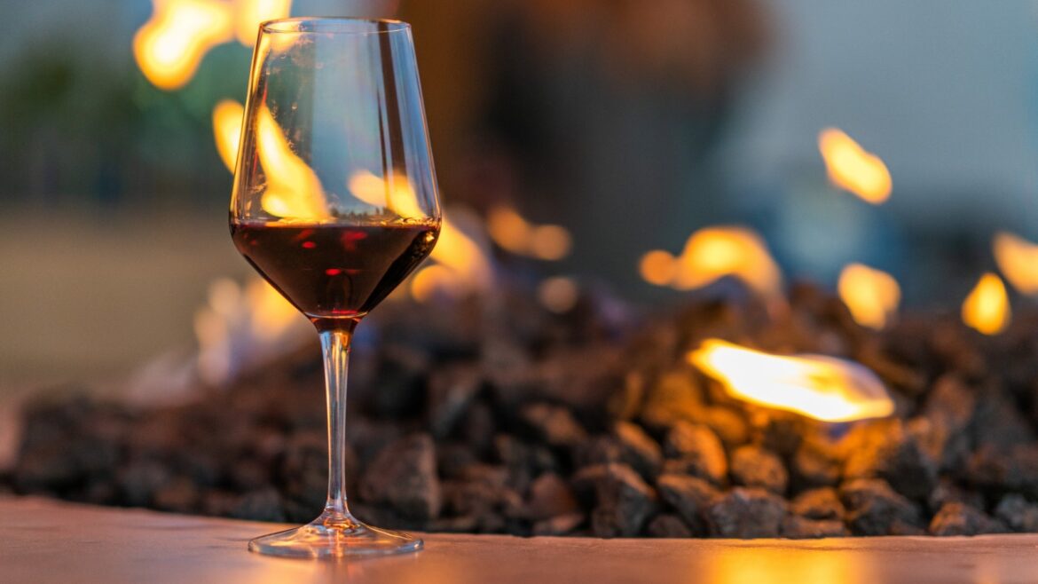 A glass of red wine sits dramatically in front of a flaming background.