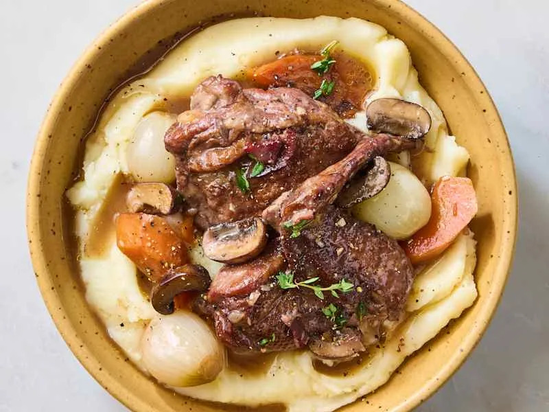 Tender lamb chops served over creamy mashed potatoes with carrots, mushrooms, and pearl onions in savory gravy.