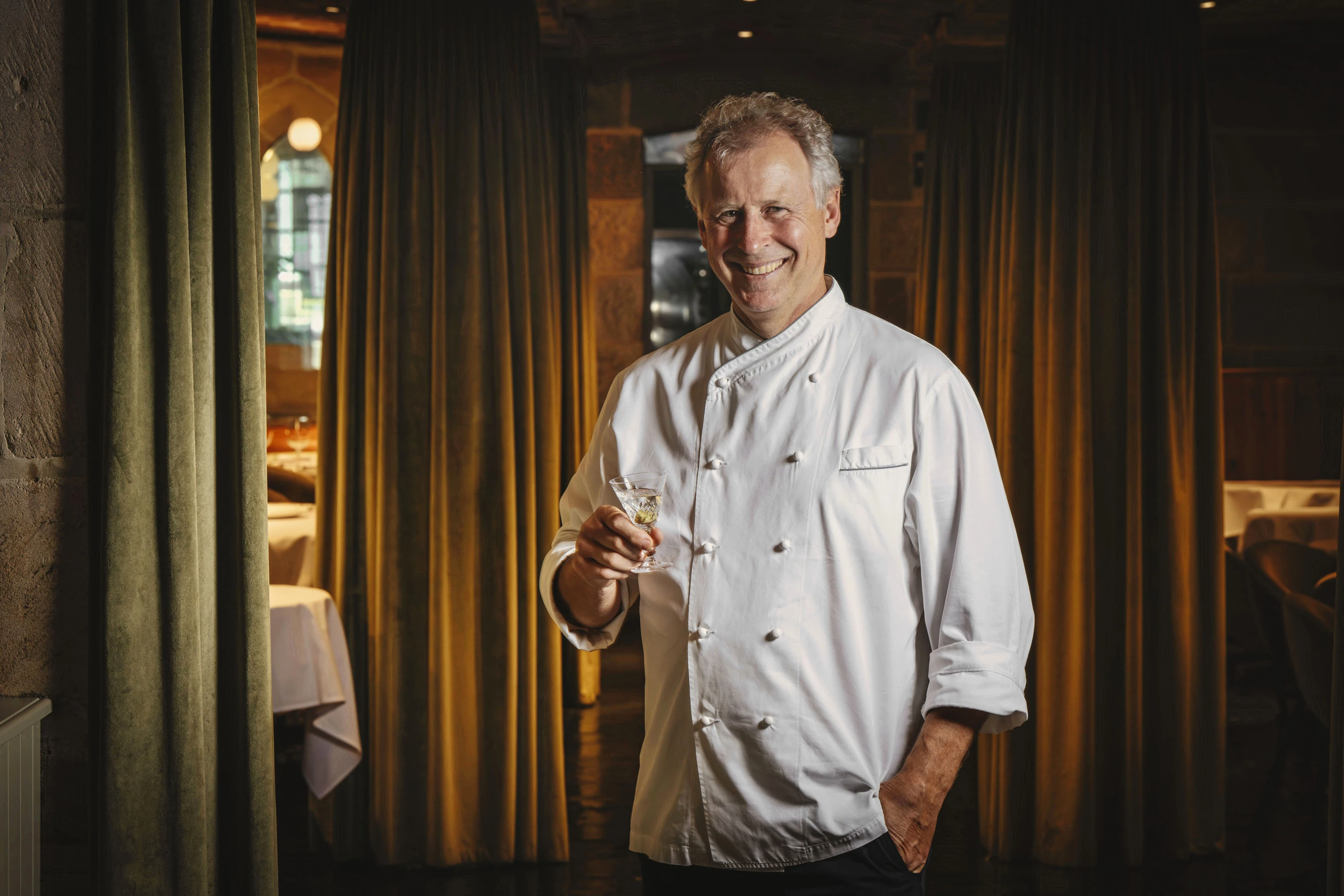A chef standing with a glass of wine