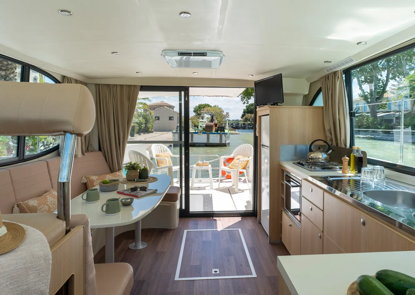Interior of a river cruise boat on the Canal du Rhône à Sète, featuring a kitchen, dining area, and view of the canal from the deck.