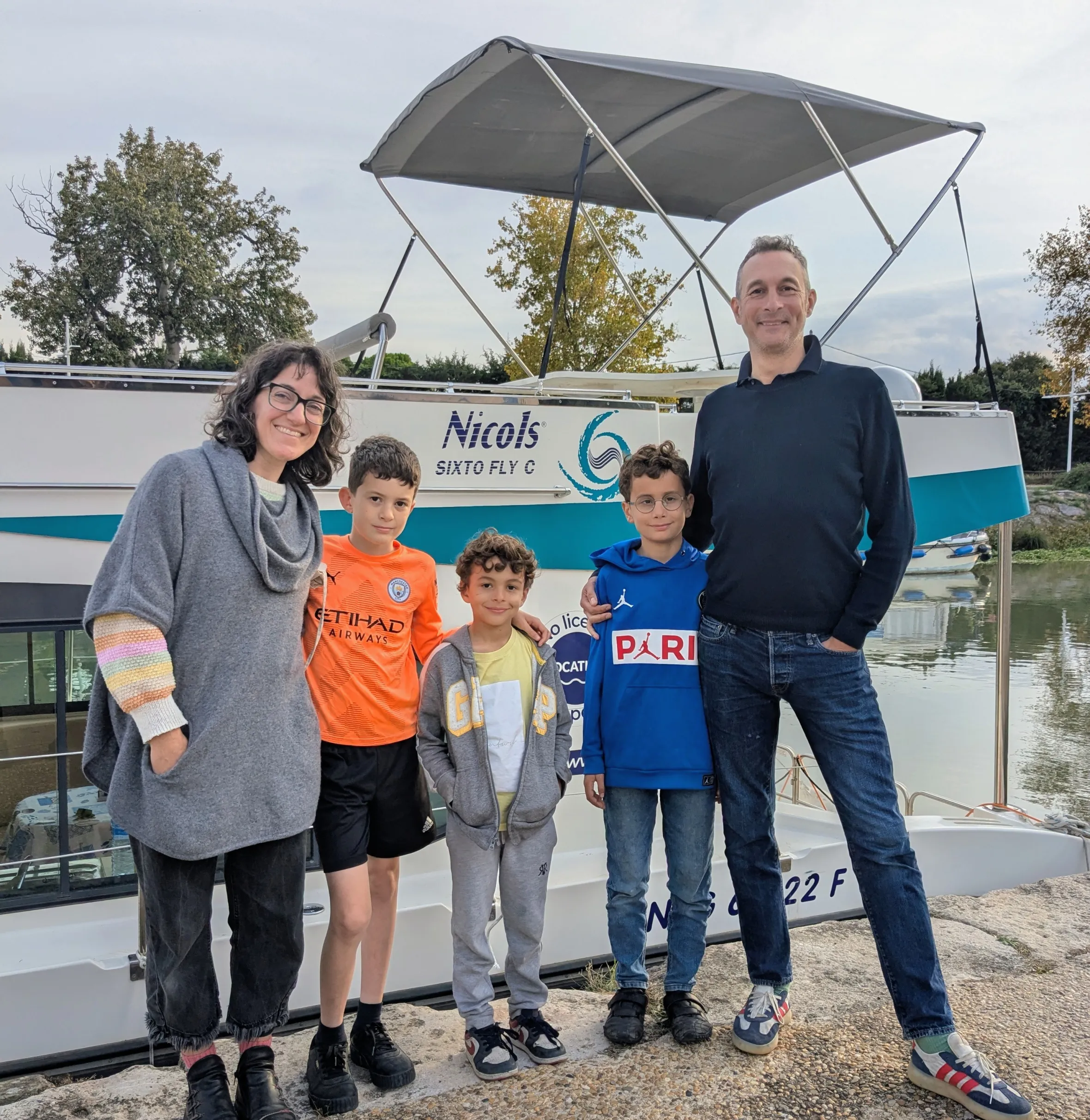 A family of five posing in front of a boat labeled "Nicols SIXTO FLY C".