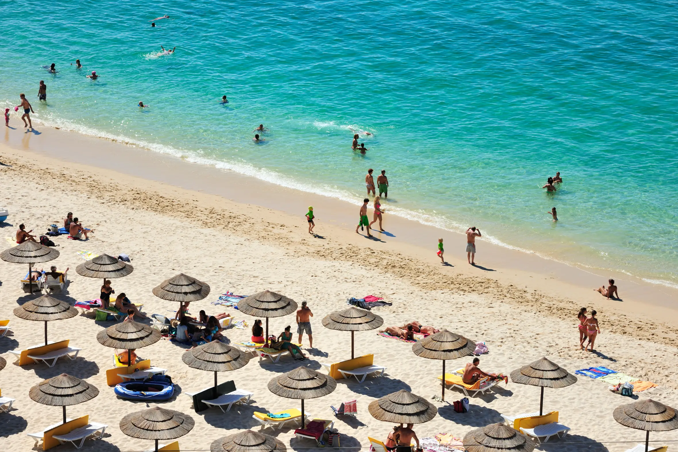 Aerial view of Galapos beach in Arrabida Natural Park, Portugal, showing people swimming and sunbathing.