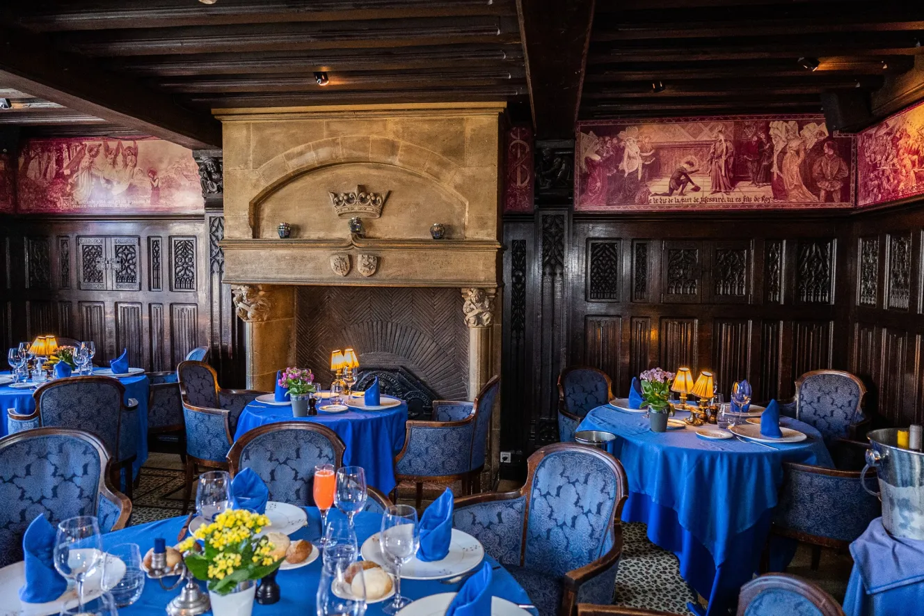 Interior of La Couronne restaurant with set tables and a large fireplace.
