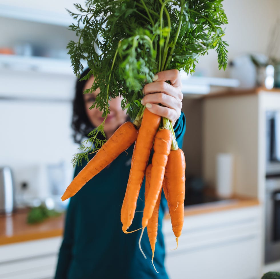 a person in a cozy kitchen holding up a fresh bunch of carrots, emphasizing health and simplicity