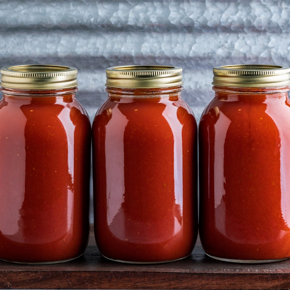 three jars of homemade water bath canned crushed tomato sauce made from homegrown tomatoes on a wooden table and industrial background