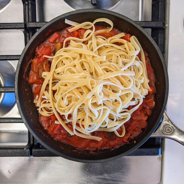 Linguine pasta arranged over a tomato-based sauce in a frying pan.