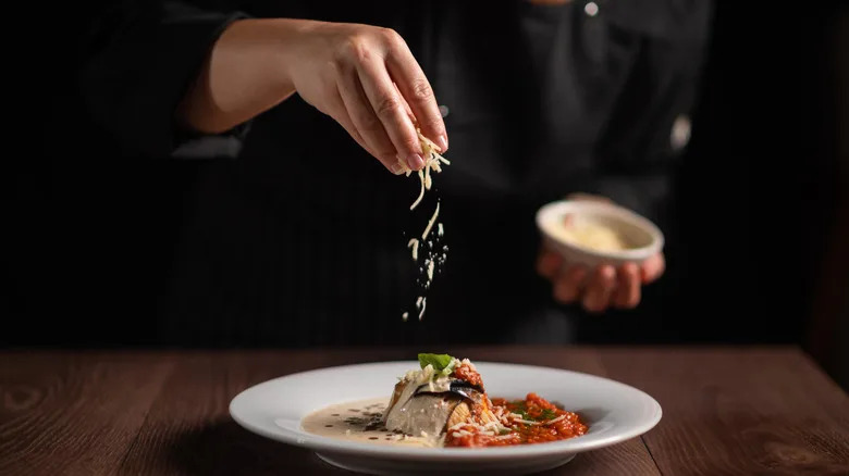 Closeup of chef sprinkling cheese over sauce-covered entree