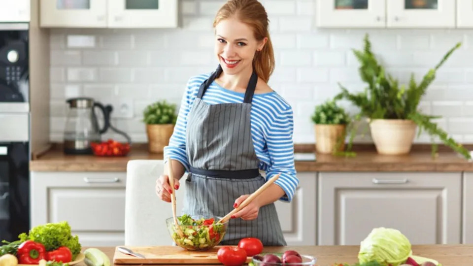 Happy woman preparing vegetable salad in the kitchen