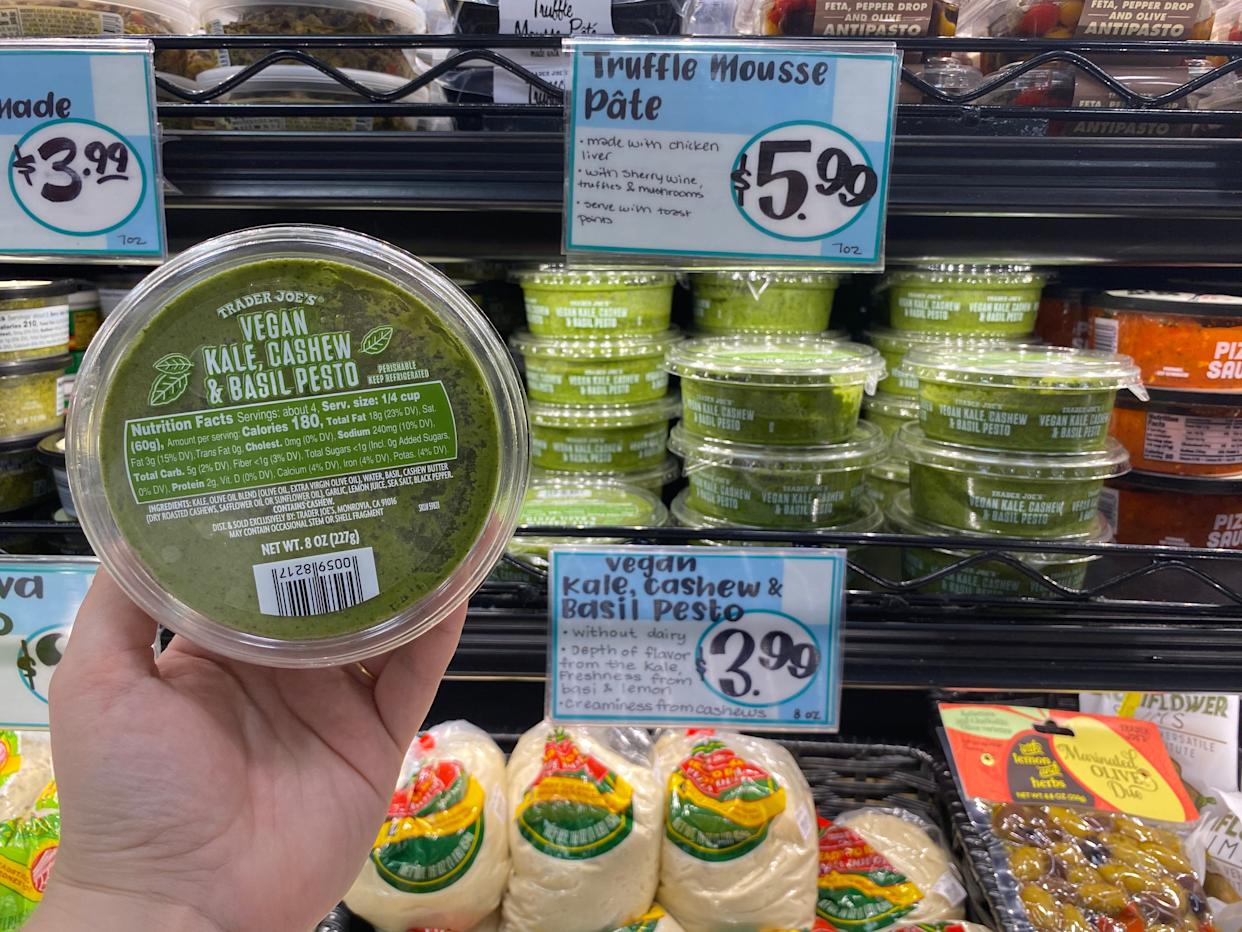 hand holding a container of vegan pesto from trader joes in front of the dips fridge