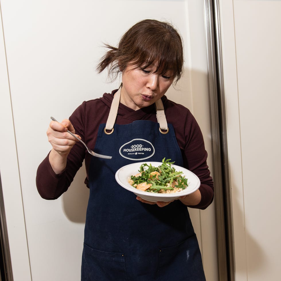 A person holding a bowl of shrimp risotto with arugula while wearing an apron.