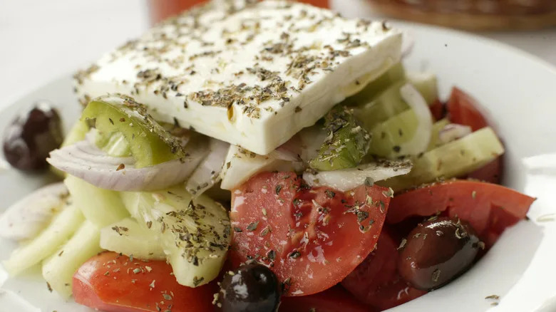 A Greek salad topped with a slice of feta cheese