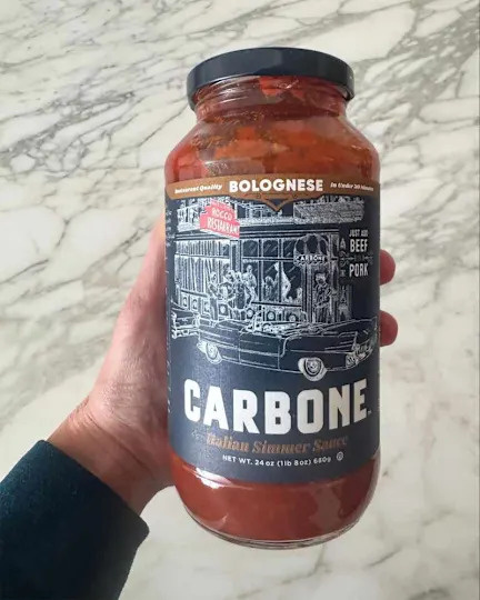 Someone holding jar of Carbone pasta sauce.