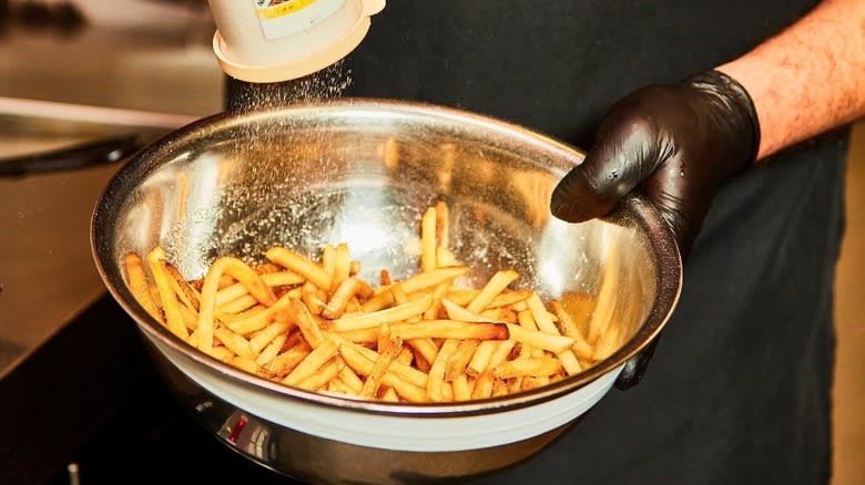 Hands shaking seasoning on Smashburger fries in a bowl