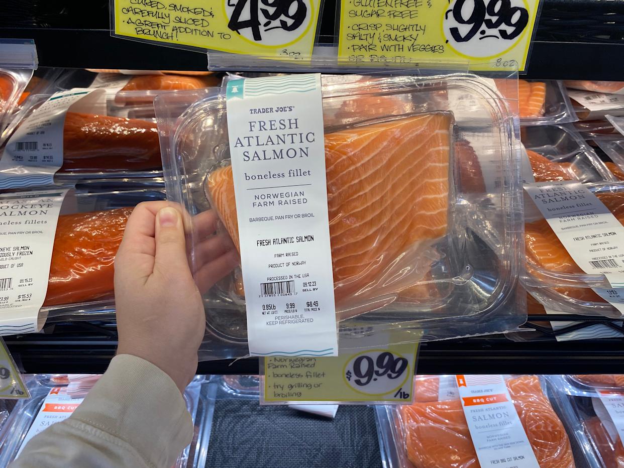 hand holding a pack of Norwegian salmon in front of the fish fridge at trader joes