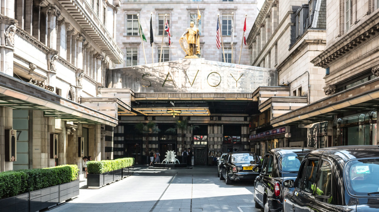 Classic London taxis queue outside imposing marble entrance of hotel Savoy in London