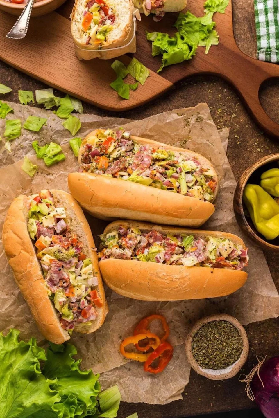 Three chopped Italian sandwiches on waxed paper with toppings around them.