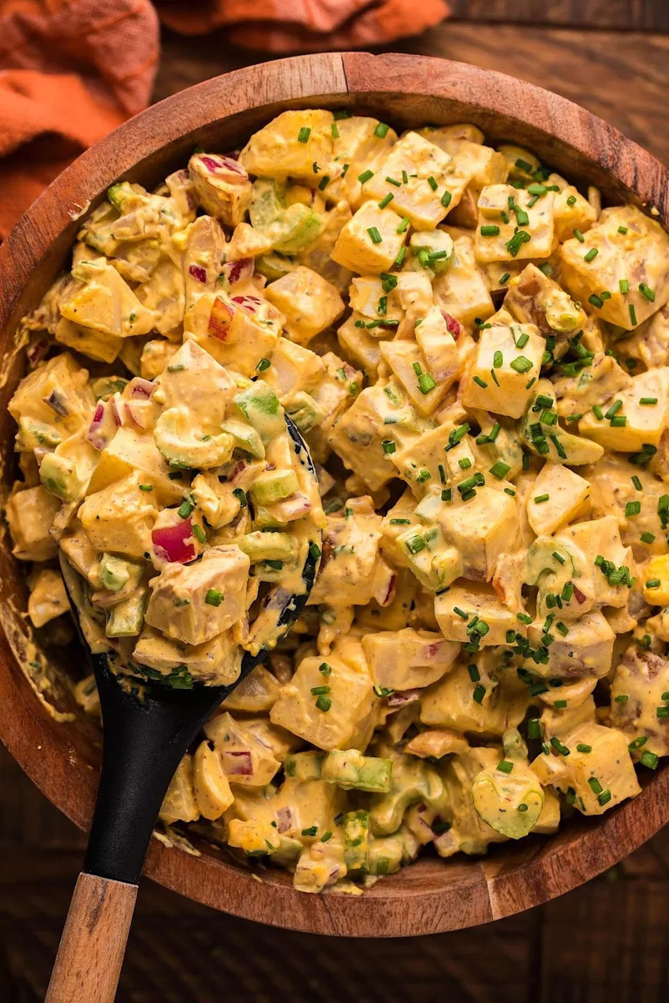 A wooden bowl with smoked potato salad and a spoon lifting a scoop.