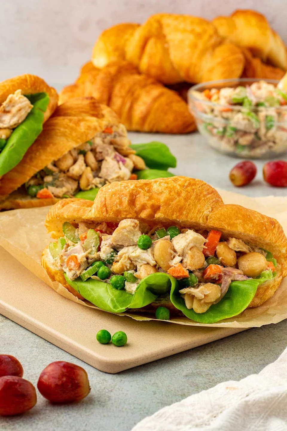 Rotisserie chicken salad sandwich with more croissants and salad behind it.