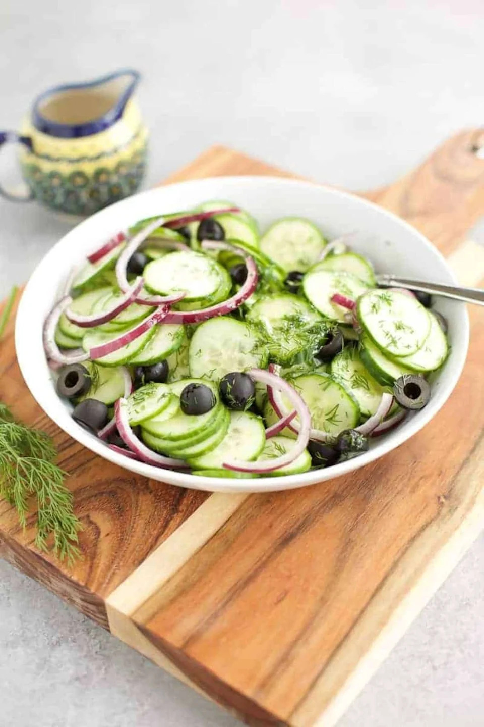 Cucumber salad with black olives and red onions in a white bowl on a cutting board.