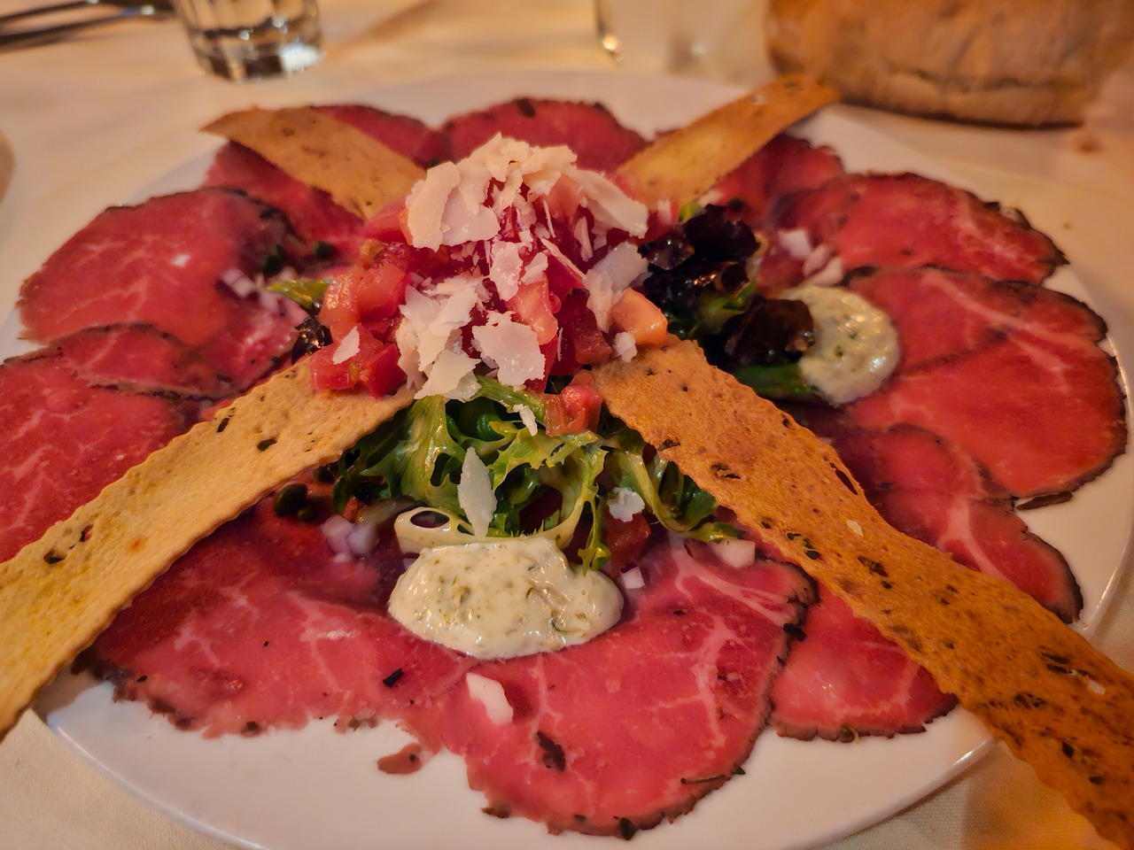 A plate of beef carpaccio topped with salad greens and crackers