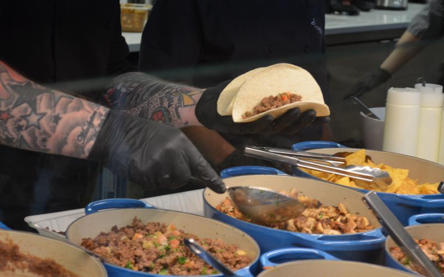 The worker holds the taco shells and spoons in the ingredients.
