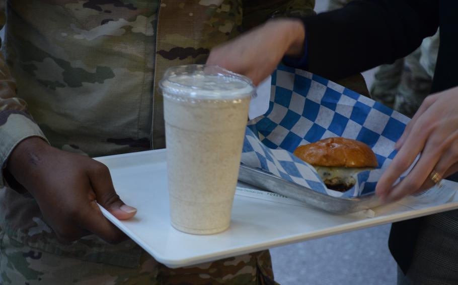 A soldier holds his tray, with a burger and a shake on it.