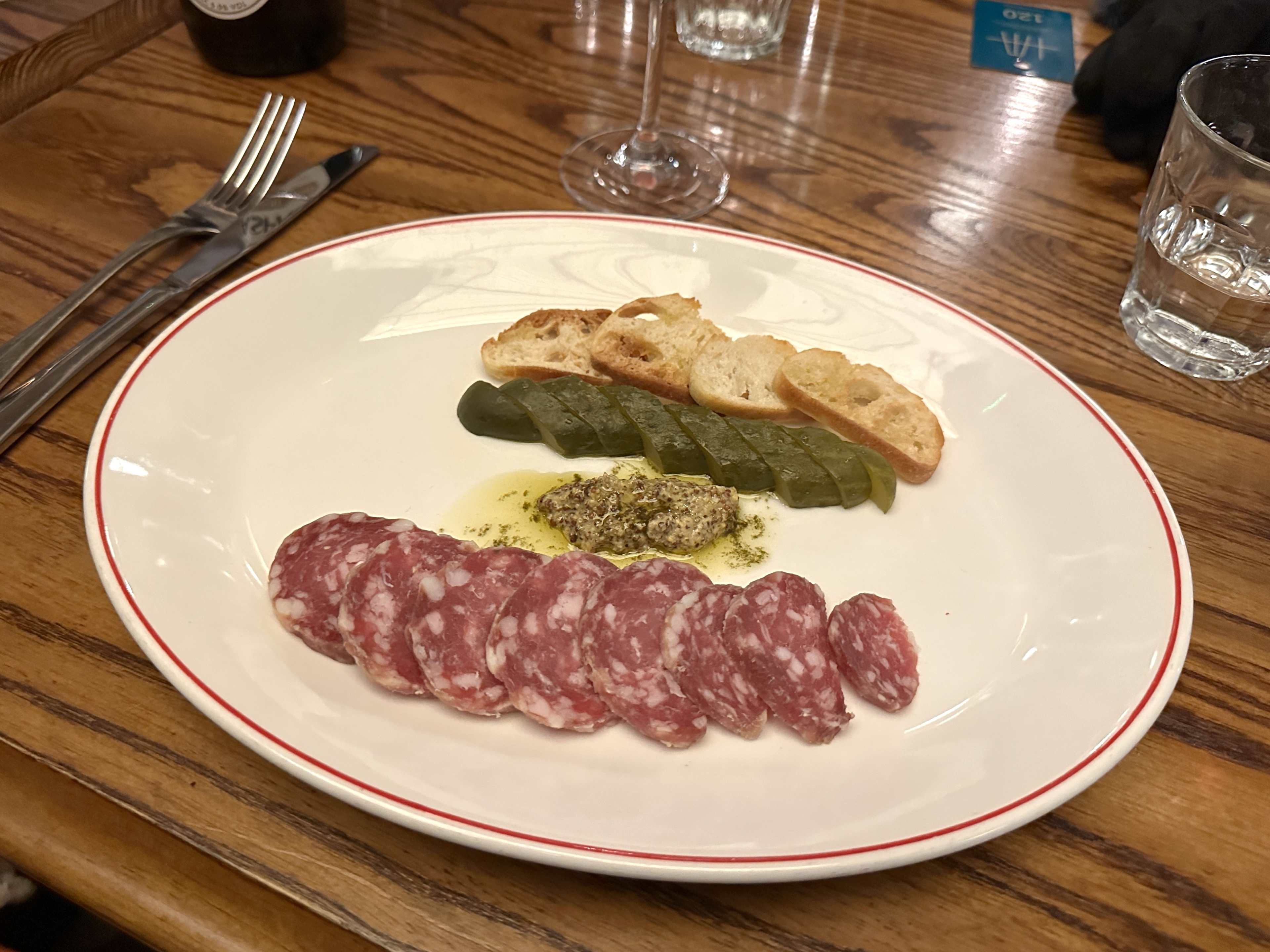 Sauccison, mustard, cornichons, and little croutons on a white plate at Marceline.