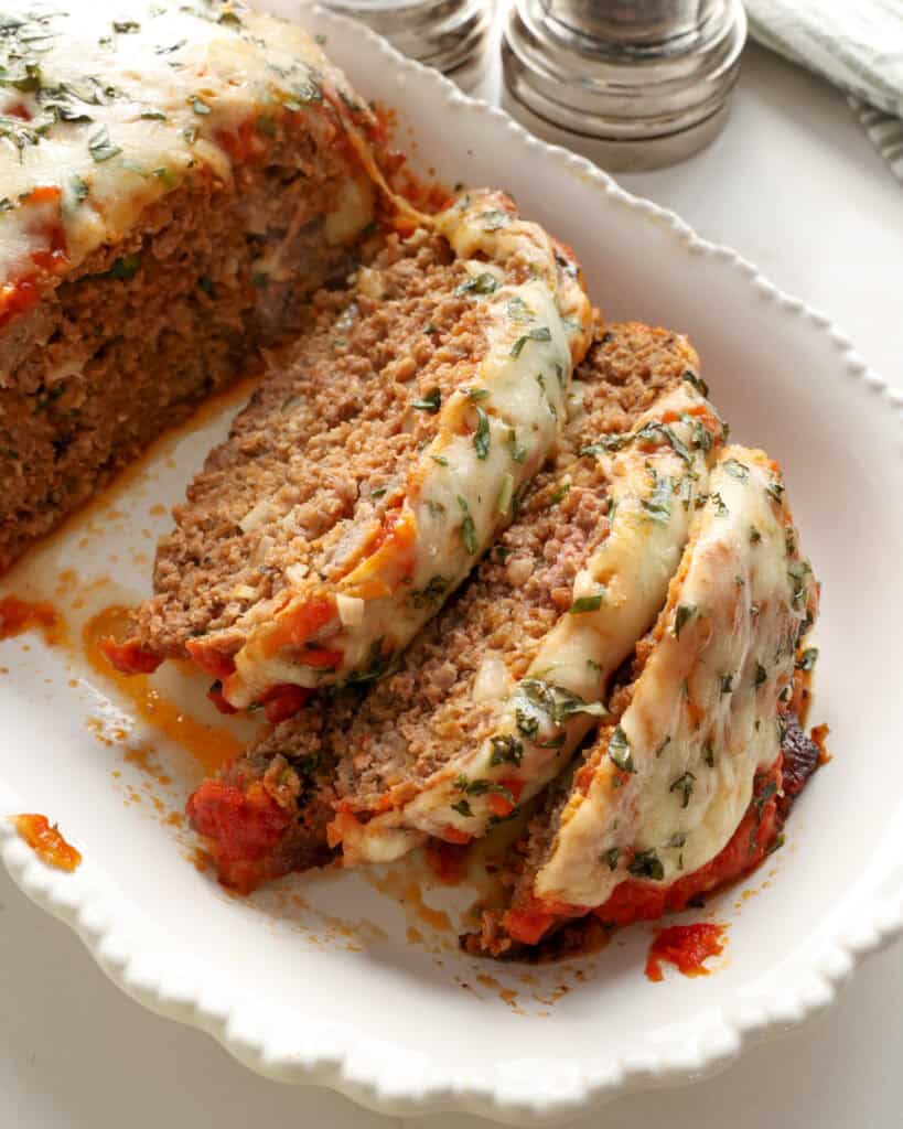 Sliced Italian meatloaf on a white serving platter with a salt and pepper shaker in the background. 