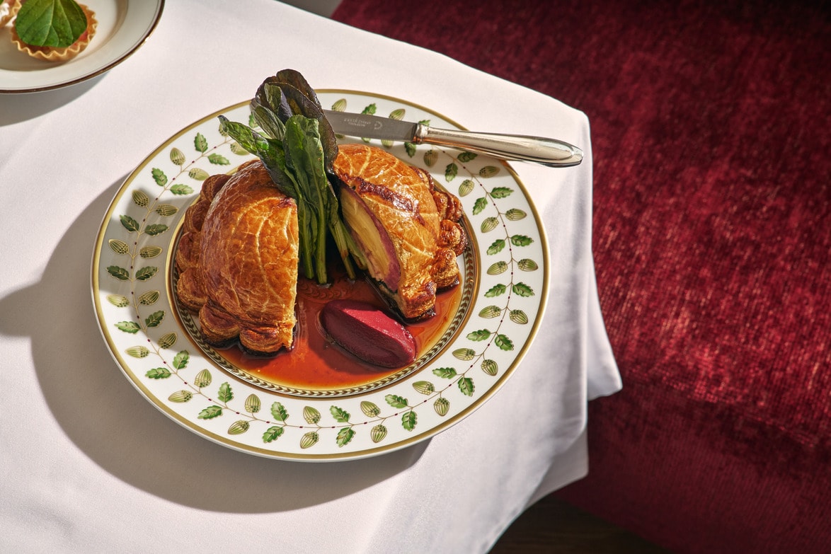 Elegant plate with a perfectly baked beef Wellington, garnished with greens and beet, on a white tablecloth.