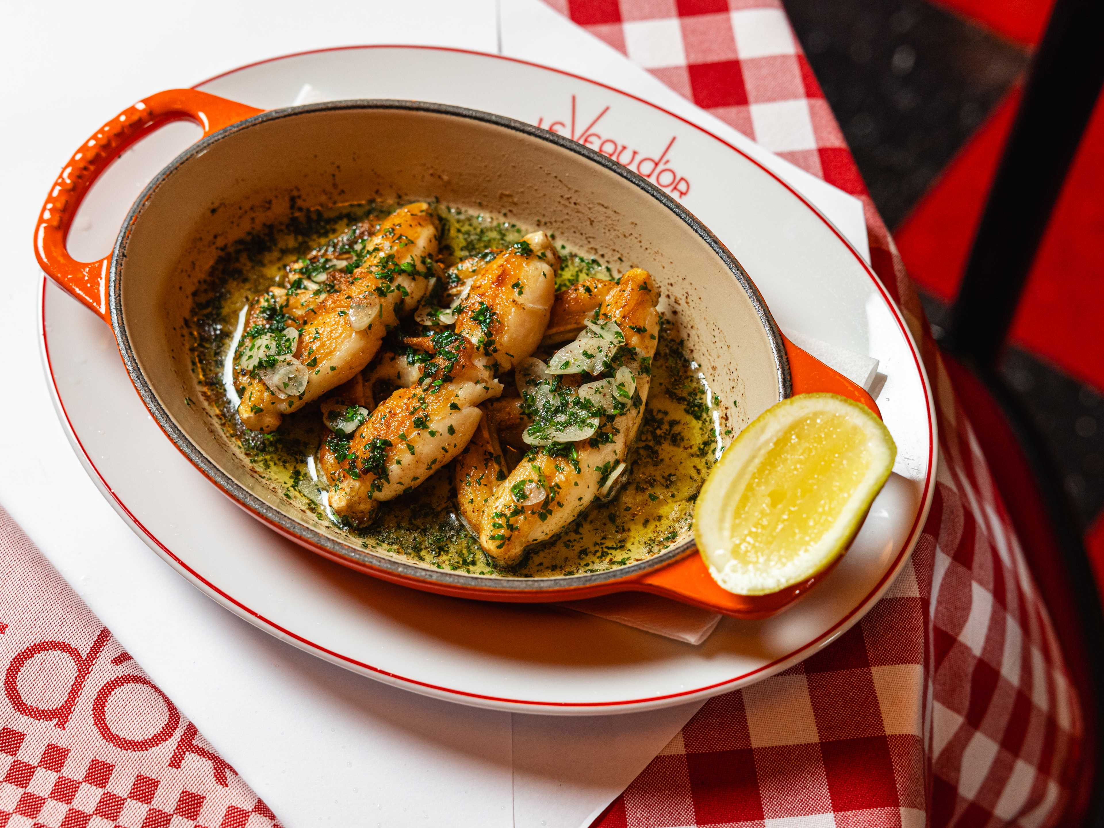 frog legs in a casserole served with lots of garlic butter and a lemon wedge