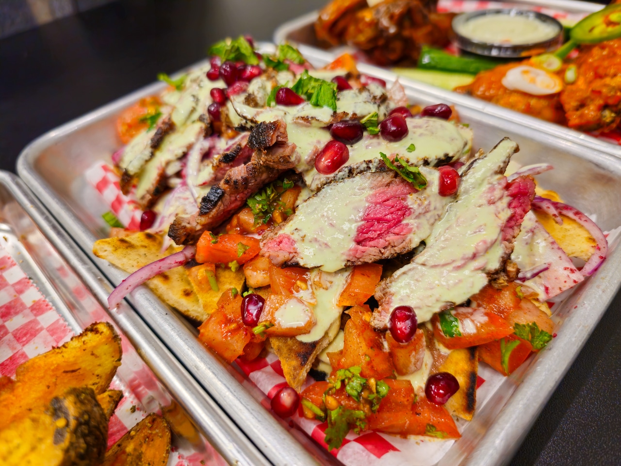A platter of pita chip nachos, topped with steak and a creamy sauce.